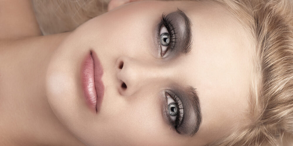 beauty close up portrait of a laying blonde with grey eyes, smokey eyes make up and soft pink glossy lips