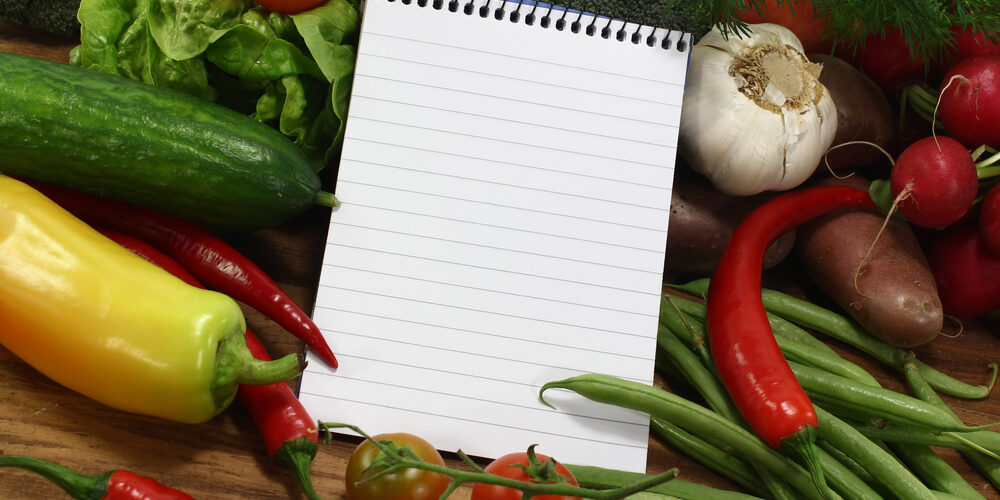 little ruled shopping list with vegetables on a wooden background