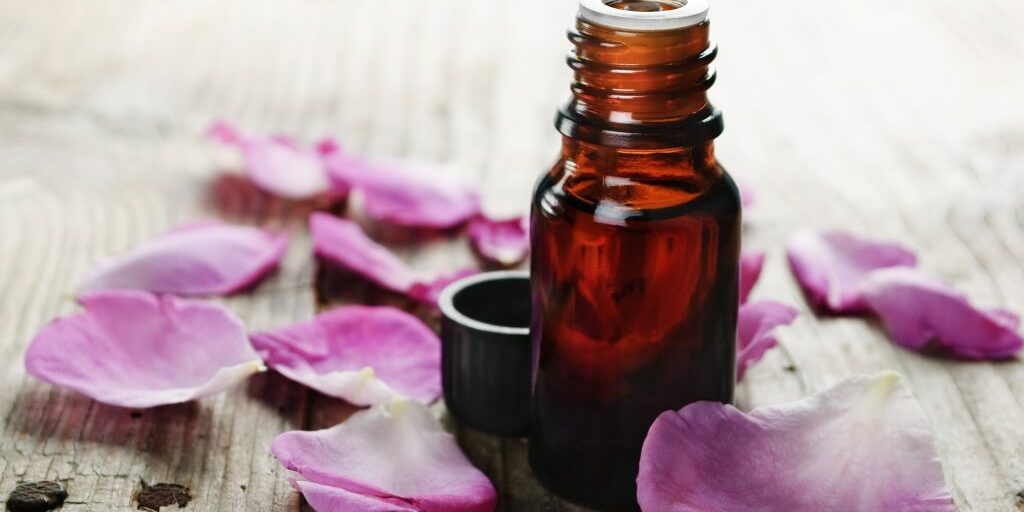Essential oil with rose petals on wooden background